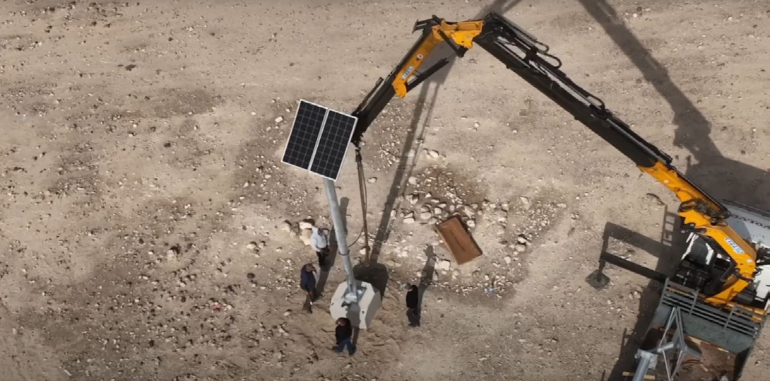 Aerial photo of an installation crew erecting a solar-powered camera pole at the archaeological site with a crane, with no trenching visible